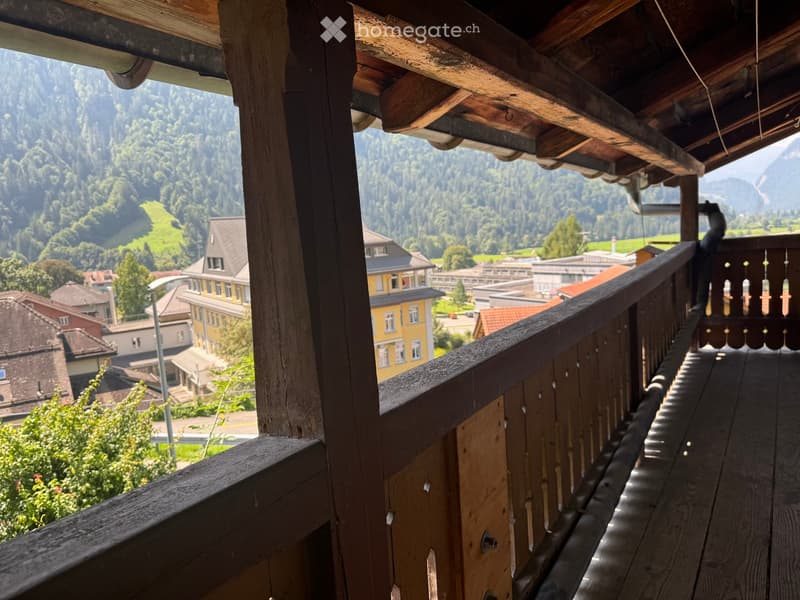 Wooden balcony with railing, overlooking a town and mountainous landscape.