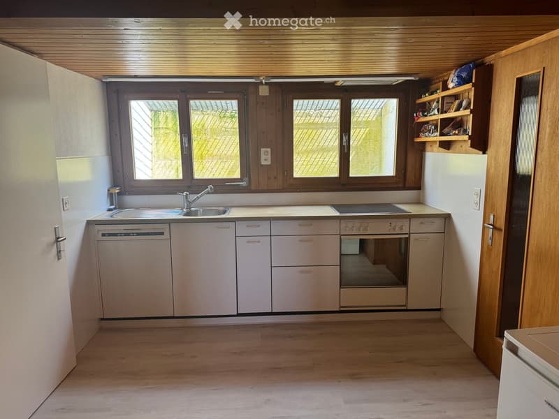 Modern kitchen with light-colored cabinets, stainless steel appliances, and wooden flooring. Features a sink, dishwasher, oven, and refrigerator.