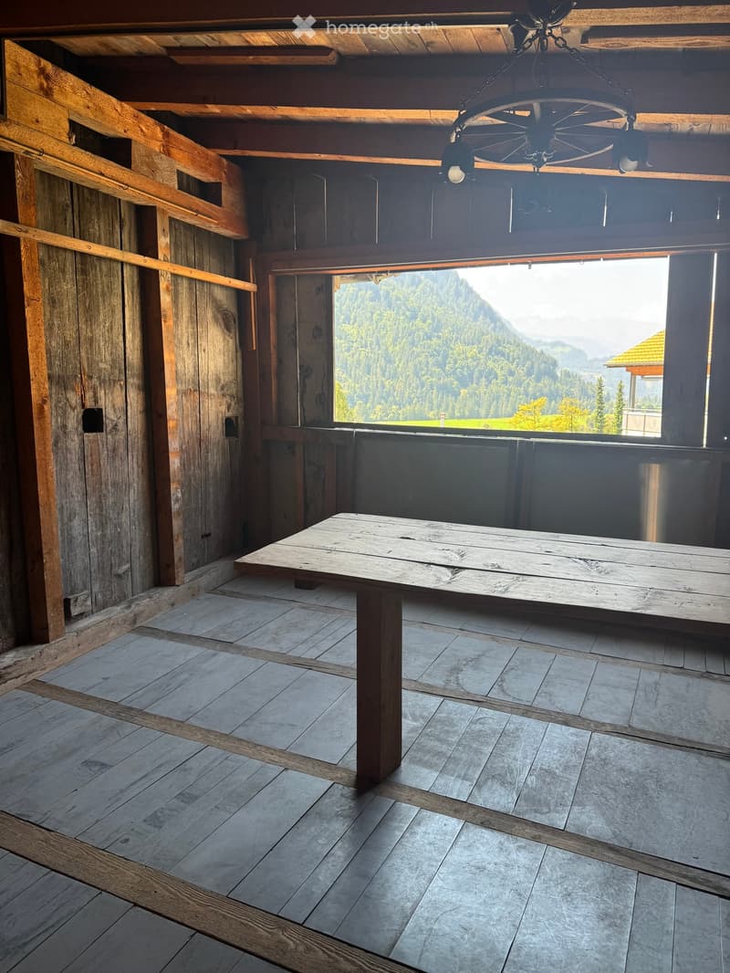 A rustic wooden room with a large wooden table, exposed wooden beams, and a scenic mountain view through large windows.