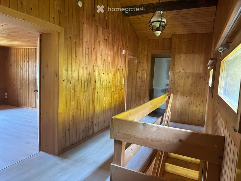 Empty wooden interior with exposed beams, wooden walls, and a staircase leading upwards.