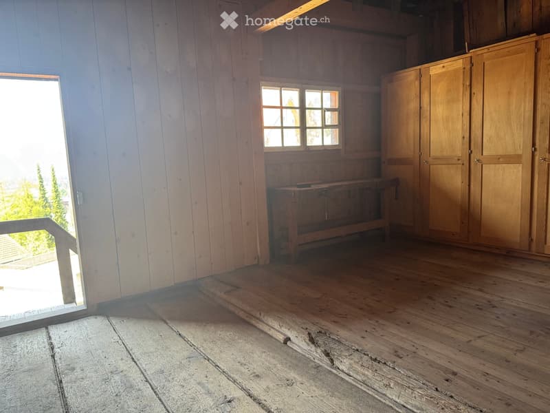 Empty room with wooden walls and floor, a small window, and a wooden bench against the wall.