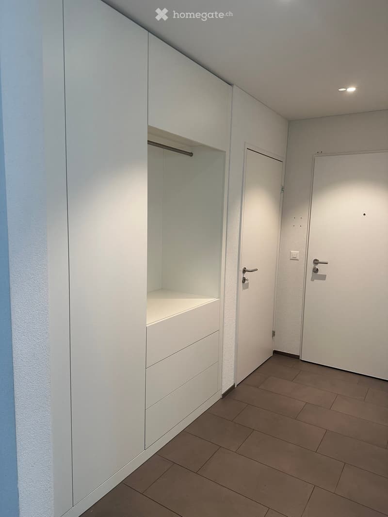 Empty hallway with white walls, tiled floor, built-in closet with glass door, and two closed doors.