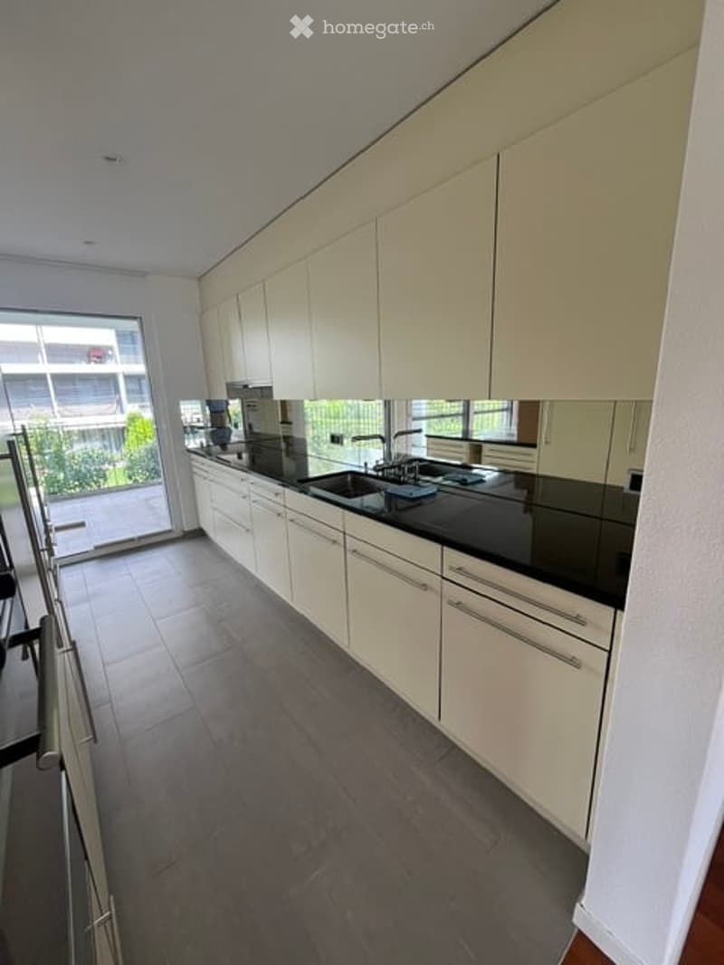 Modern kitchen with white cabinets, black countertops, and stainless steel appliances. Features a large window with a view of the balcony and surrounding buildings.