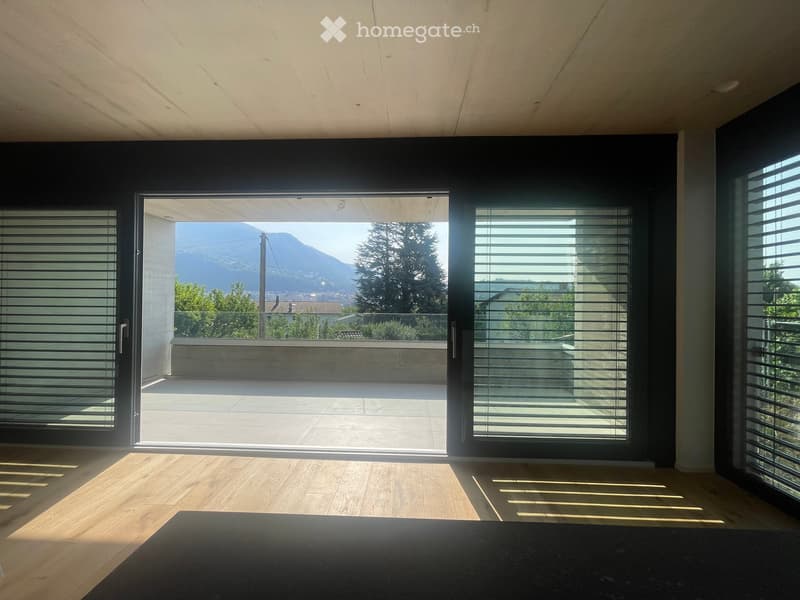 Bright, modern room with wooden flooring, large sliding glass doors opening to a balcony with a scenic mountain view.