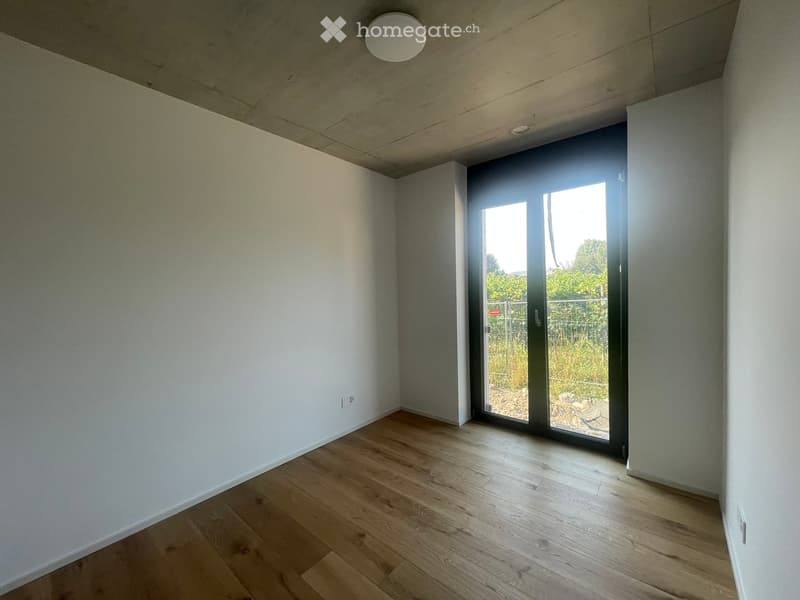 Empty room with light wooden flooring, white walls, and a large sliding glass door leading to an outdoor area.
