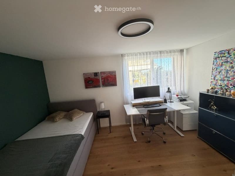 A multi-functional room with a bed, desk, and office chair. The room features a modern design with a large window, colorful artwork, and a sleek desk setup.