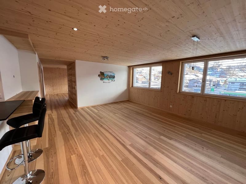 Modern, minimalist room with wooden floors and walls, large windows, and a bar area with stools.