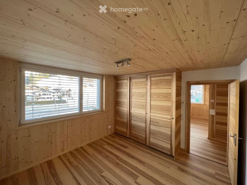 Empty room with wooden walls, ceiling, and floor, large window with blinds, and a closed wooden closet.