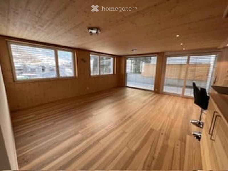Bright, empty room with wooden flooring and large windows, featuring modern recessed lighting and a sliding glass door leading to an outdoor area.