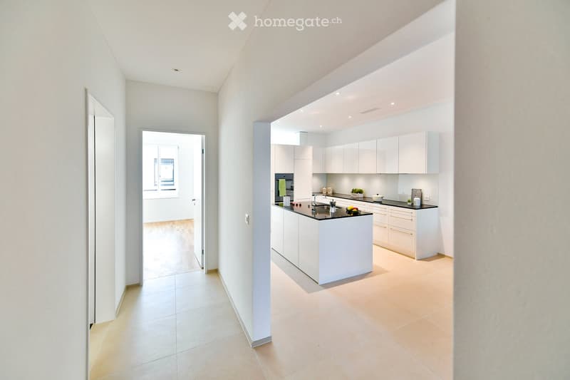 Modern, minimalist kitchen with white cabinets, a central island, and a sleek black countertop. The space is bright with natural light and features a clean, contemporary design.