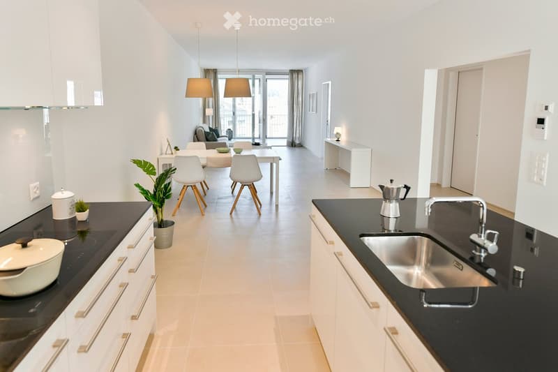 Modern kitchen and living area with white cabinets, black countertops, pendant lights, and a small seating area with a couch and chairs.