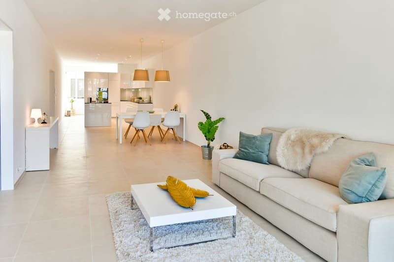 Modern living and dining area with white furniture, a sofa with a fur throw, a coffee table with a decorative leaf, a dining table with four chairs, and a small kitchen area with cabinets and a pendant lamp.