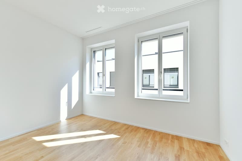 Empty room with white walls, wooden floor, and large windows allowing natural light to enter.
