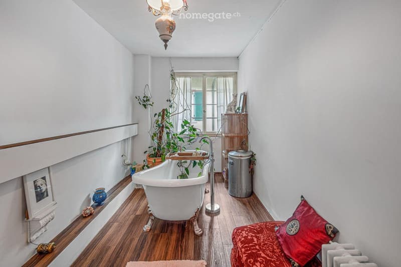 Bathroom with a freestanding bathtub, wooden flooring, radiator, and decorative items including a plant and picture frame.