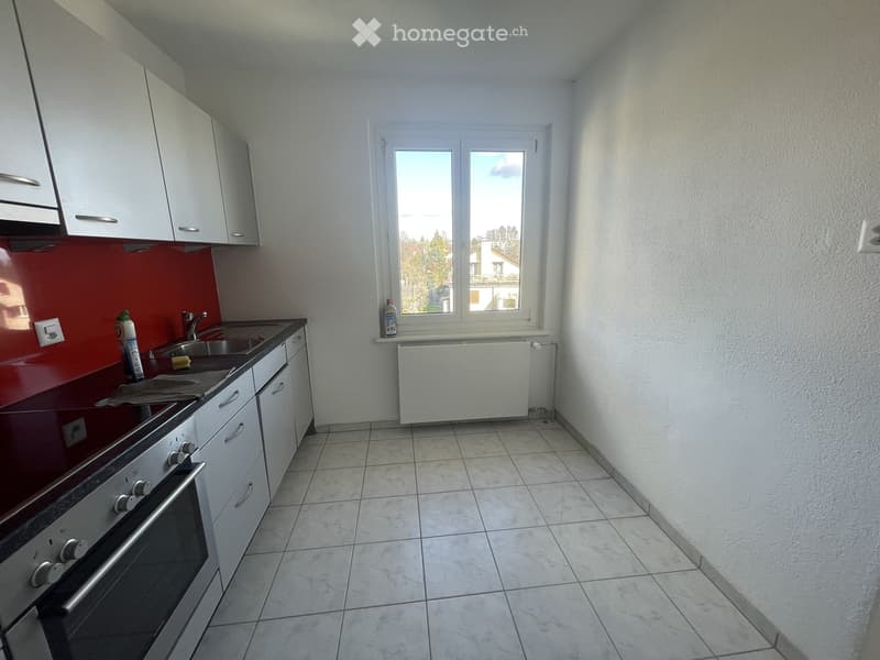 Modern kitchen with white cabinets, stainless steel oven, sink, and a window overlooking a residential area.
