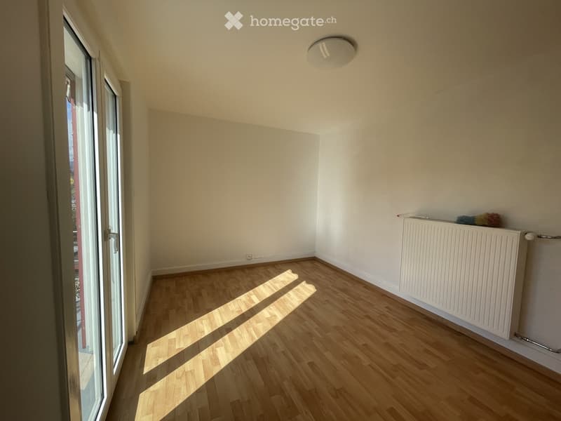 Empty room with wooden flooring, white walls, a radiator, and a large window with blinds.