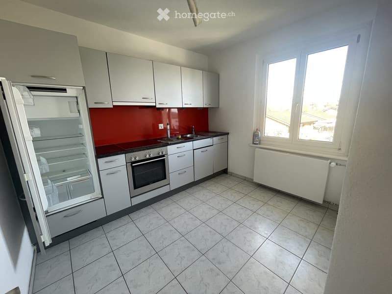 Modern kitchen with white cabinets, stainless steel appliances, tiled floor, and large windows.