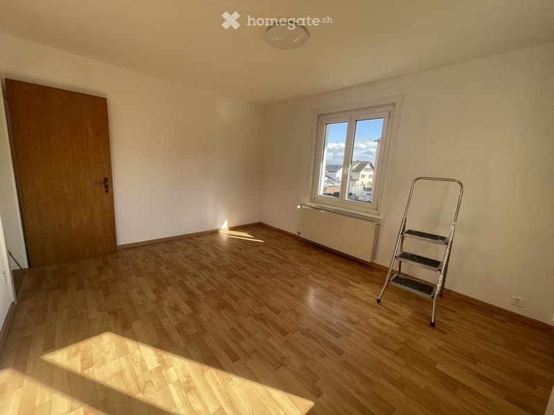 Empty room with wooden flooring, white walls, a window, a door, and a ladder in the corner.