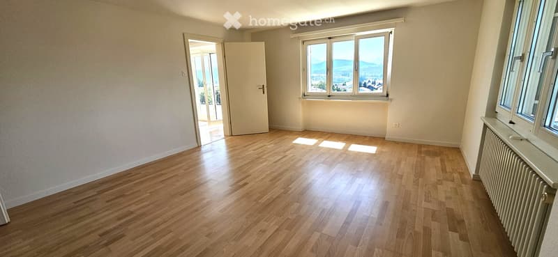 Empty room with wooden flooring, large windows, and a door leading to a balcony.
