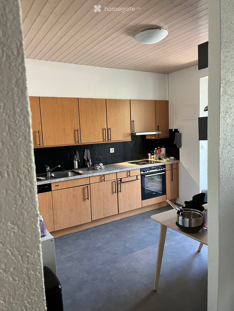 Modern kitchen with wooden cabinets, granite countertop, stainless steel appliances, and a small wooden table with a pot.