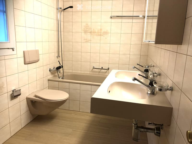 Modern bathroom with a bathtub, double sink, and a toilet.
