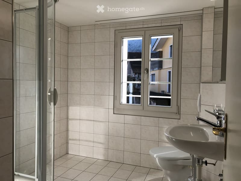 Tiled floor, glass shower enclosure, white sink, toilet, white tiles, window