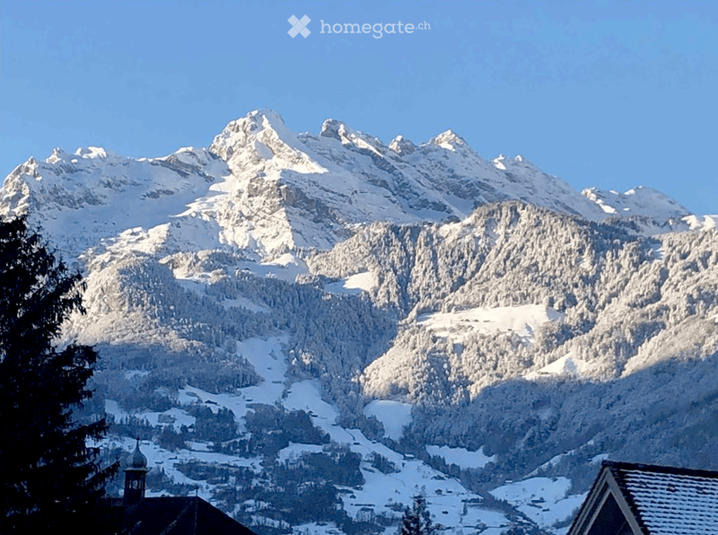 Snowy mountain peaks and valleys, with a village nestled in the valley below. The landscape is covered in a blanket of snow, creating a serene and picturesque winter scene.