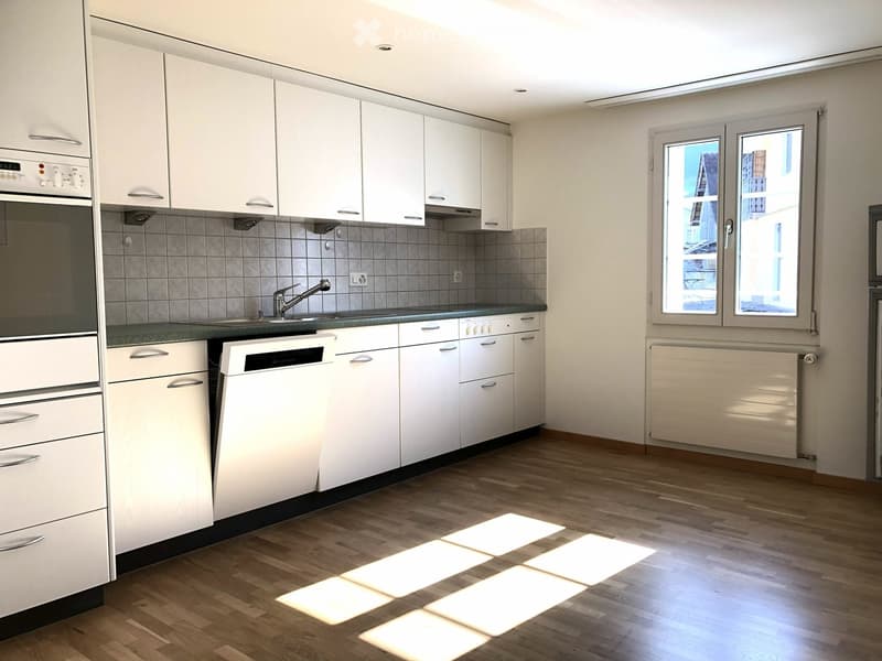 Modern kitchen with white cabinets, green countertops, built-in oven, dishwasher, sink with faucet, tiled backsplash, wooden floors, window with natural light.