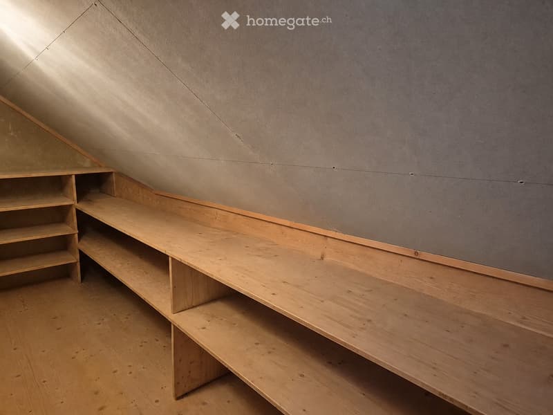 An empty attic space with wooden flooring and built-in wooden shelving units along the slanted ceiling.
