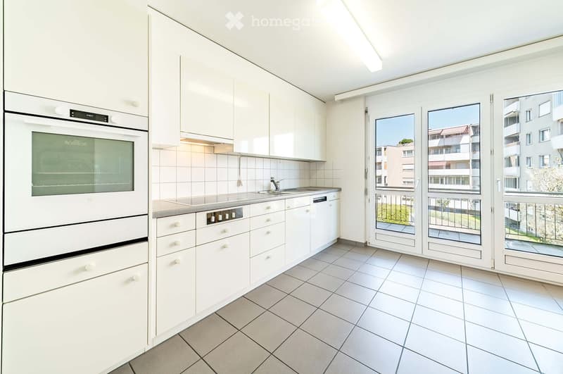 Modern kitchen with white cabinets, stainless steel appliances, and a large window overlooking a balcony.