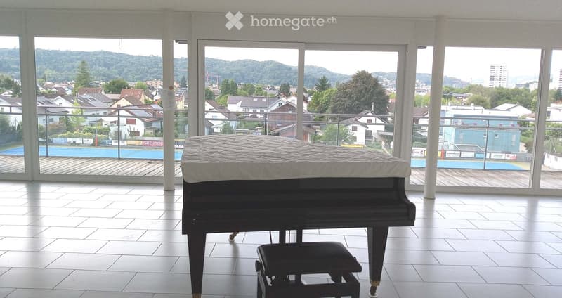 Bright room with large windows offering a scenic view, featuring a grand piano and a matching bench.