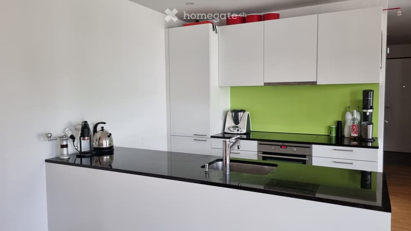 Modern kitchen with white cabinets, black countertops, stainless steel appliances, and a green backsplash.