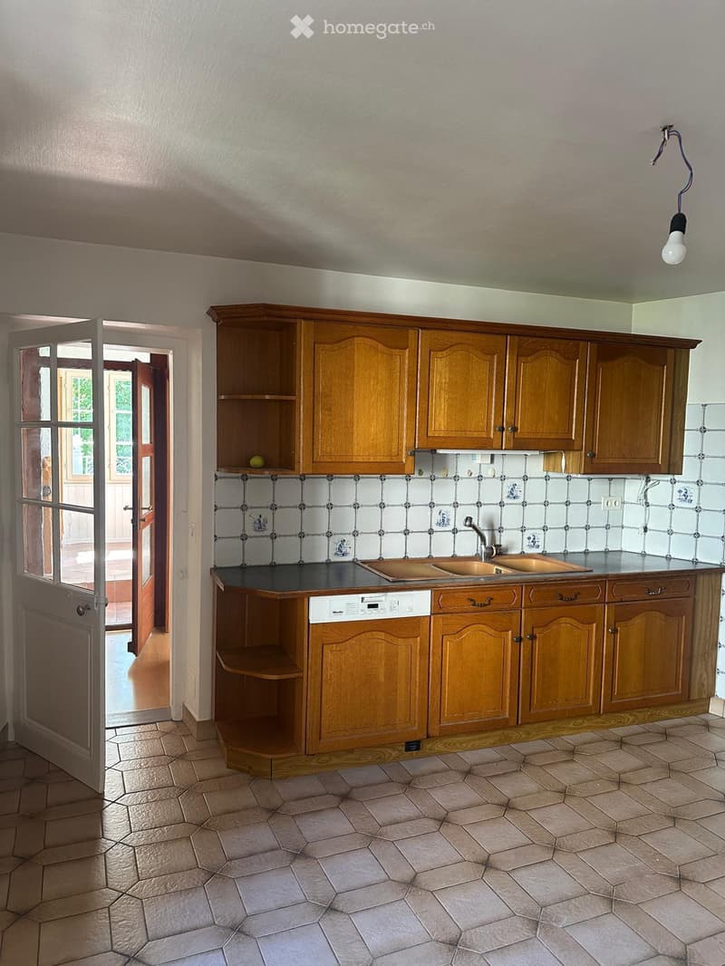 Empty kitchen with wooden cabinets, tiled backsplash, and a sink area. The space features a tiled floor and an open doorway leading to another room.