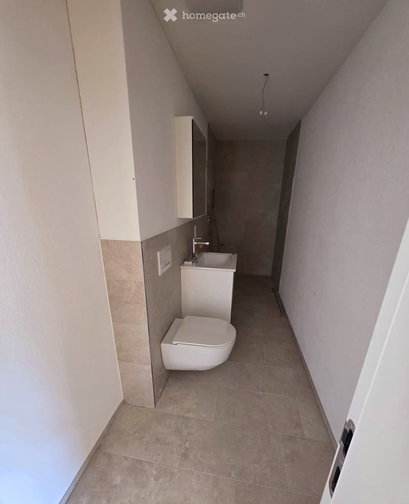 Modern bathroom with a toilet, sink, and cabinet, featuring beige tiled walls and floor.