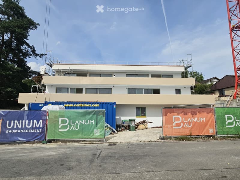 Modern two-story building under construction with scaffolding, banners, and construction materials visible.