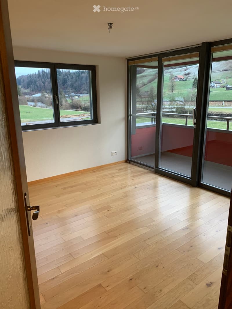 Empty room with wooden flooring, large windows, and sliding glass doors leading to a balcony with scenic views.