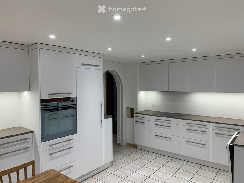 Modern kitchen with white cabinets, stainless steel appliances, and a wooden dining table with a chair.