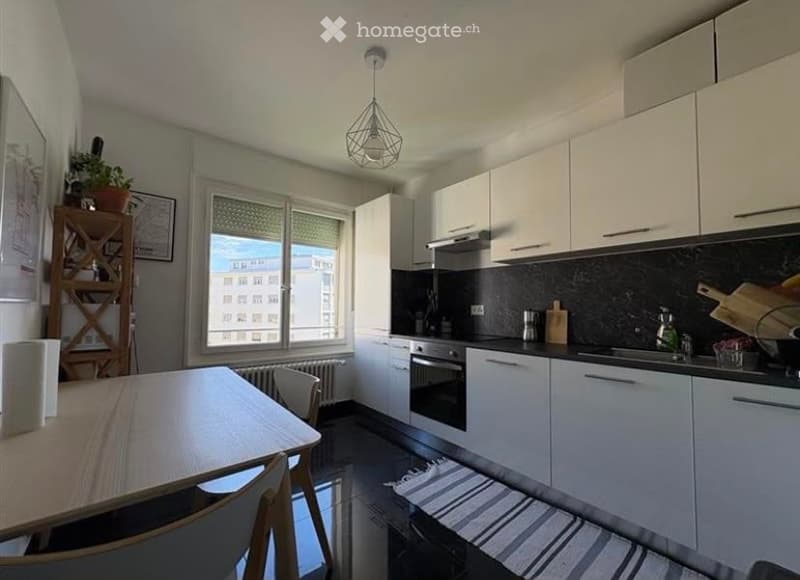 Modern kitchen with white cabinets, a dining table with chairs, a window with a view, and various appliances including an oven and sink.