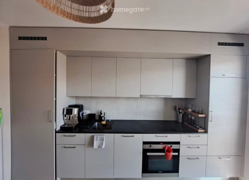 Modern kitchen with white cabinets, black countertops, and stainless steel appliances including a coffee maker, oven, and sink.