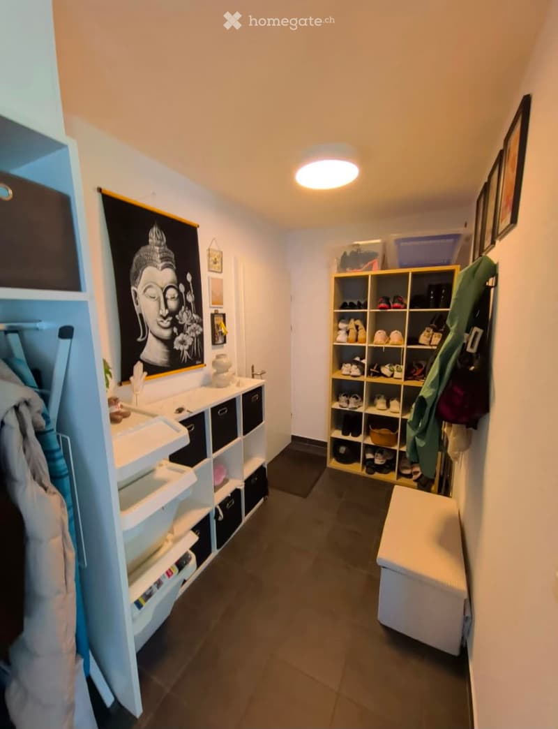 Well-lit hallway with white walls, dark tiled floor, built-in storage units, and a bench at the end.