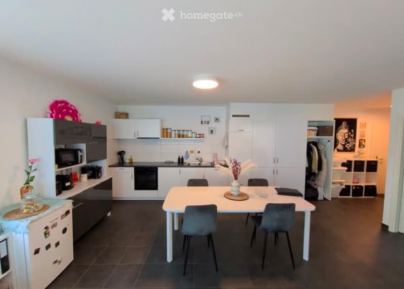 Modern kitchen and dining area with white cabinets, black appliances, a dining table with four chairs, and decorative items on shelves and counters.