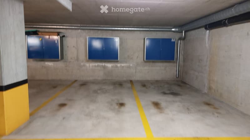 Underground parking area with concrete floors and walls, marked parking spaces, and blue storage cabinets.