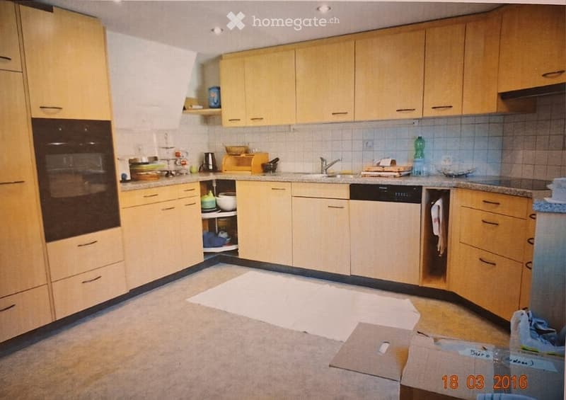 A modern kitchen with light wooden cabinets, a stainless steel oven, a dishwasher, and various kitchen items on the counter.