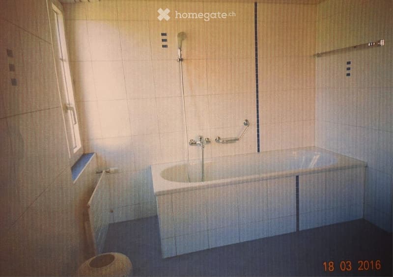 Bathroom with a bathtub, tiled walls, a window, and a handrail for safety.