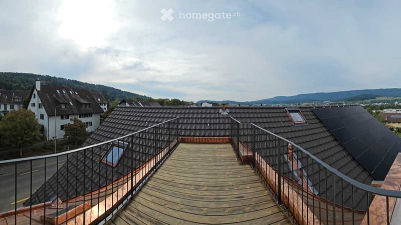 Roof terrace with wooden decking, metal railing, and scenic view of surrounding houses and hills.