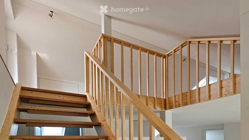 Wooden staircase with a wooden handrail and balustrade, leading to an upper level with white walls and ceiling.