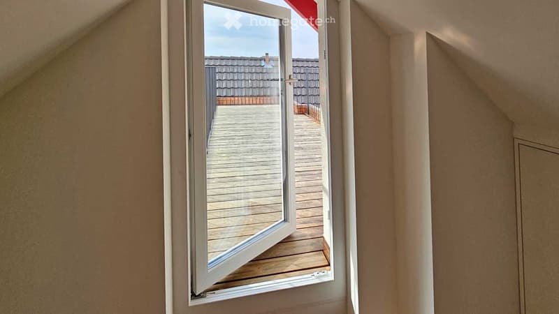 Open window leading to a wooden balcony with a view of a neighboring roof.
