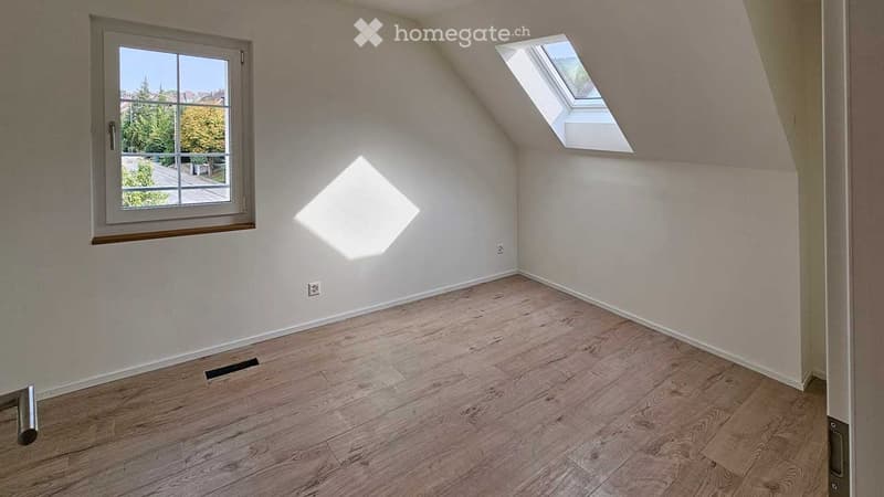Empty attic room with wooden flooring, white walls, a window, and a skylight. No furniture or equipment present.