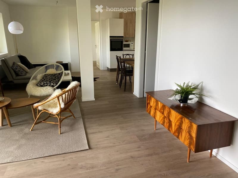 Open floor plan, modern design, wooden flooring, white walls, natural light, open kitchen area, dining table, chairs, couch, floor lamp, rug, wooden cabinet