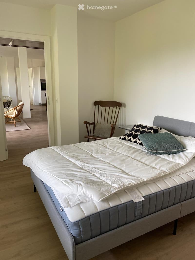large bed, wooden chair, side table, carpet, white walls, wooden floor